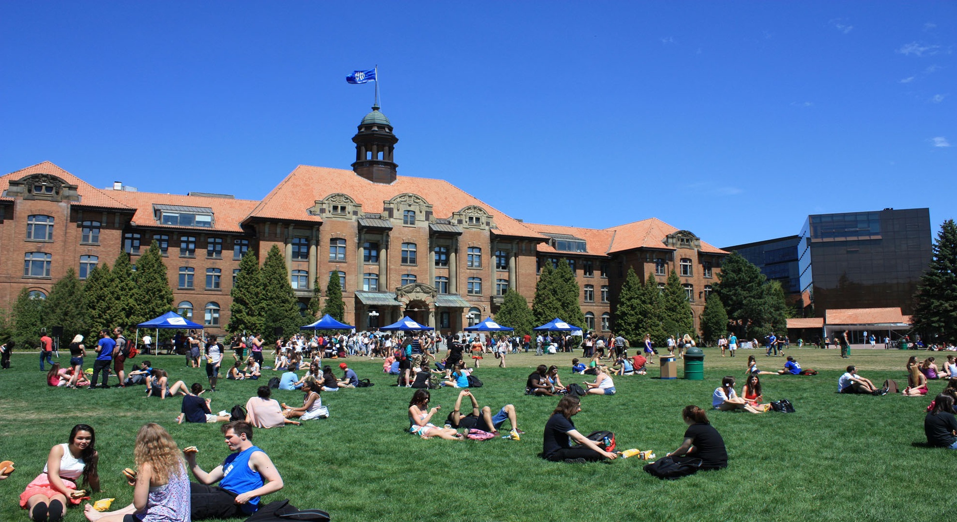 Hundreds of students sitting in the grass infront of the main John Abbott College Building